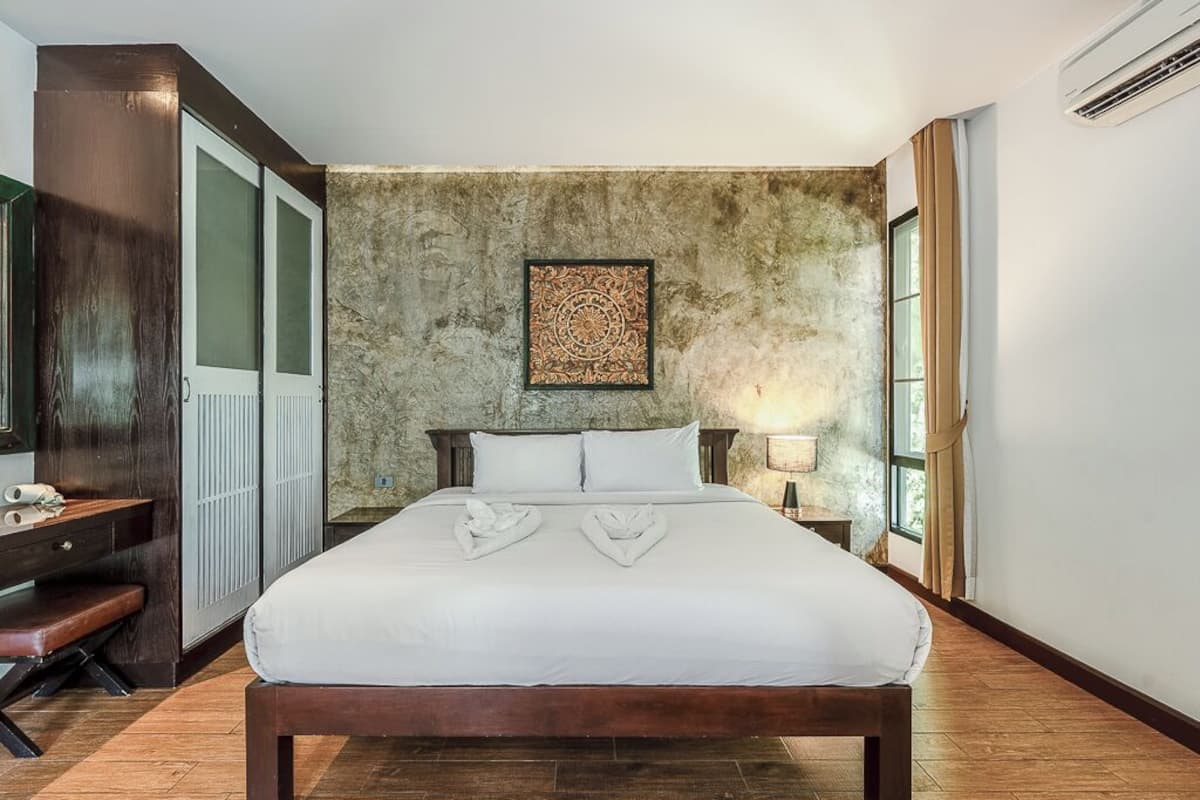 Habitación de hotel con una cama grande, un banco de madera, un escritorio y una pared de piedra con un panel decorativo.