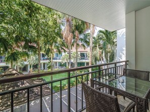 A balcony with wicker furniture, a glass table, and a view of a building with palm trees. - Coco Retreat Phuket Resort and Spa Sha+ (Chalong)