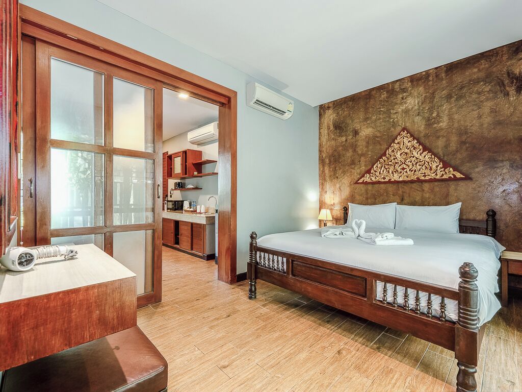 A bedroom with a wooden bed, a desk with a lamp, a wardrobe, and a wall-mounted air conditioner.