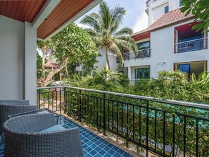 A balcony with wicker furniture, a pool, and lush tropical vegetation. - Coco Retreat Phuket Resort and Spa Sha+ (Chalong)