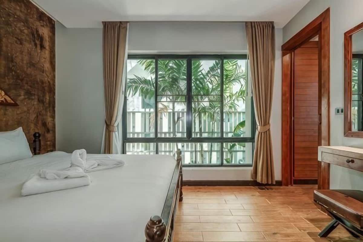 Habitación de hotel con una cama grande, piso de madera, una ventana con cortinas y una puerta de madera.