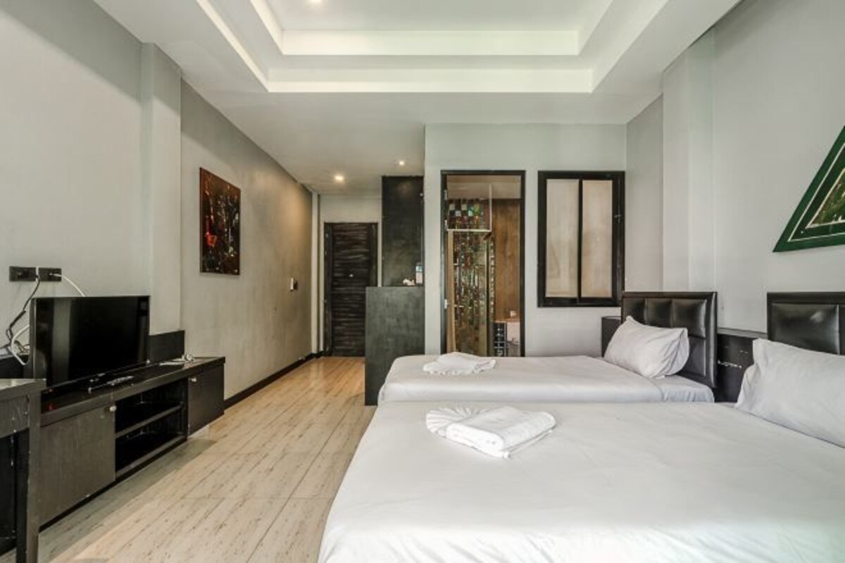 A hotel room with two beds, a TV, a desk, and a ceiling light.