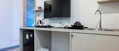 A compact kitchenette with a built-in refrigerator, a microwave, a coffee maker, a sink, and a television mounted above the counter.