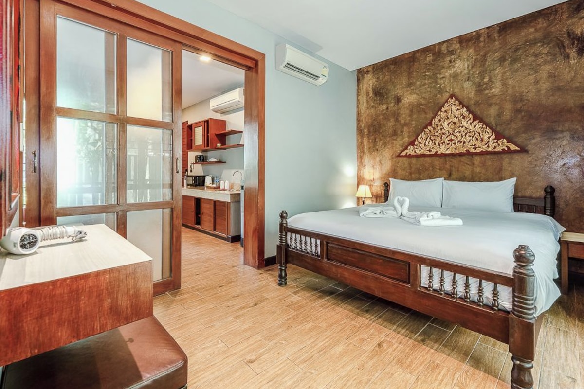A bedroom with a wooden bed, a nightstand, a desk with a lamp, and a large window.