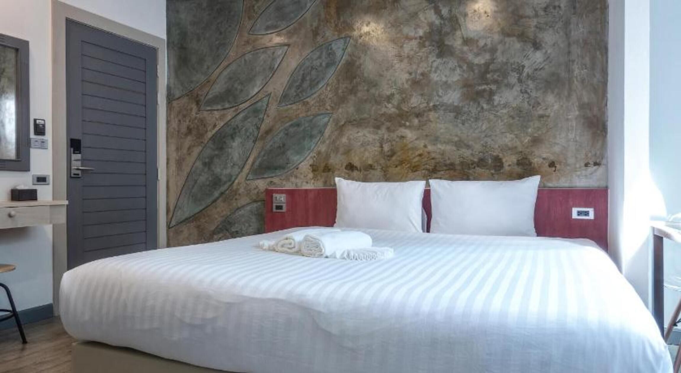 A hotel room with a bed, a wall with leaf patterns, a door, and a small table.