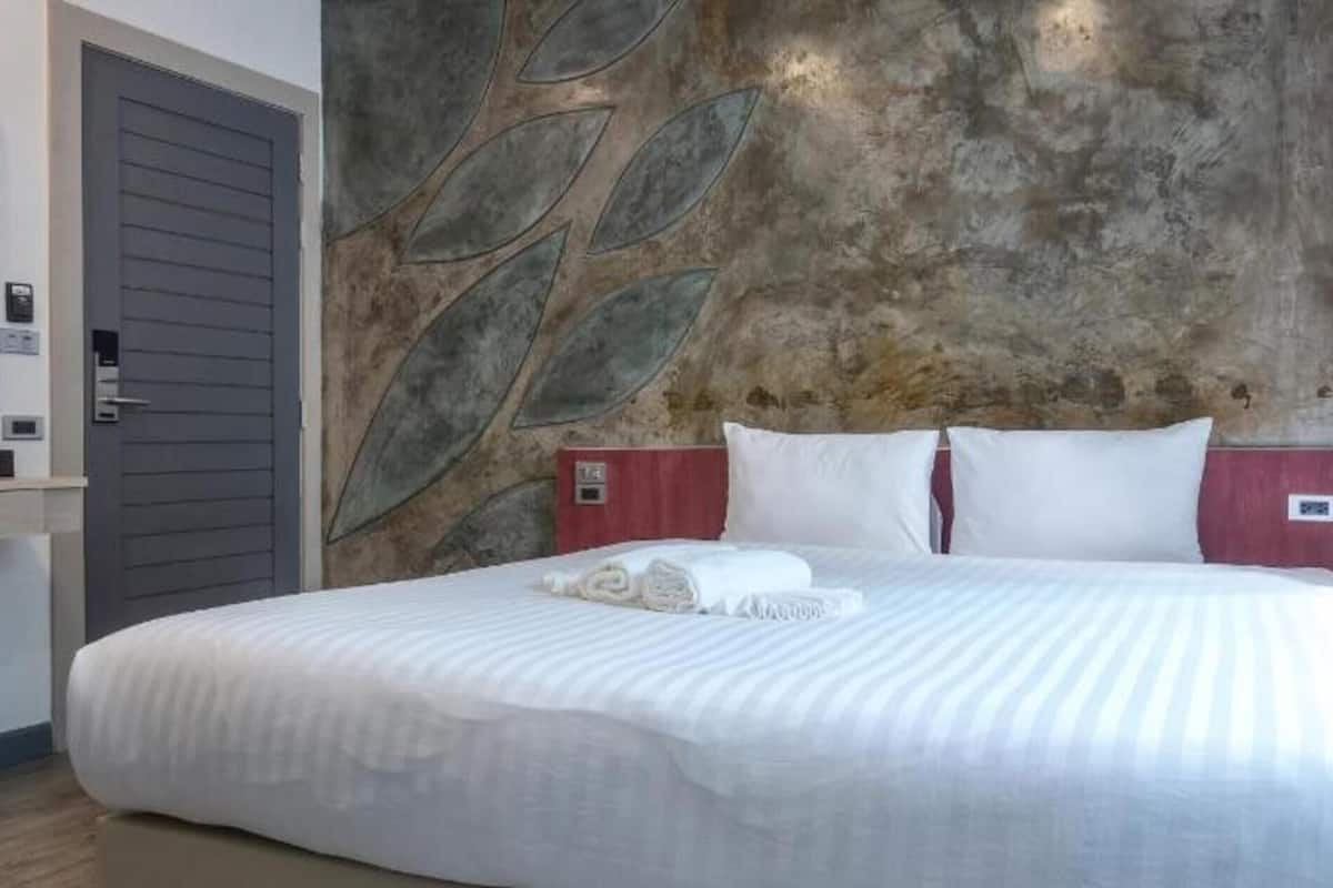 Una habitación de hotel con cama, una pared con motivos de hojas, una puerta y una mesita.