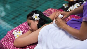 A person receiving a massage with flowers in their hair, lying on a patterned bed with a water feature in the background. - Coco Retreat Phuket Resort and Spa Sha+ (Chalong)
