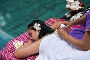 A person receiving a massage with flowers in their hair, lying on a patterned bed with a water feature in the background. - Coco Retreat Phuket Resort and Spa Sha+ (Chalong)