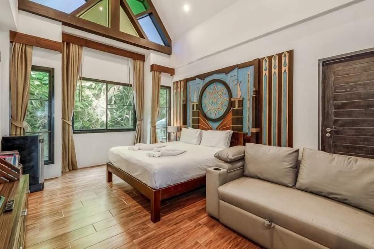 Un dormitorio con una cama, un sofá, un televisor y un ventanal grande.