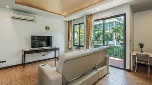 A modern living room with a sofa, a flat-screen TV, a small table, and a balcony with a view of greenery. - Coco Retreat Phuket Resort and Spa Sha+ (Chalong)