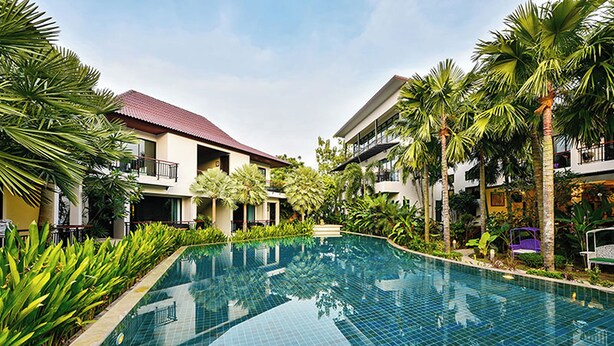 A swimming pool surrounded by buildings with balconies, palm trees, and a clear sky. - Coco Retreat Phuket Resort and Spa Sha+ (Chalong)