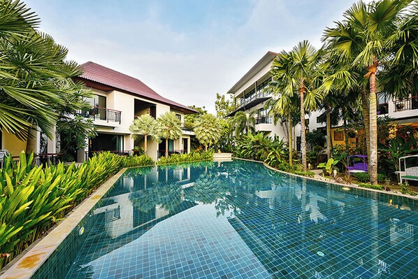 A swimming pool surrounded by buildings with balconies, palm trees, and a clear sky. - Coco Retreat Phuket Resort and Spa Sha+ (Chalong)