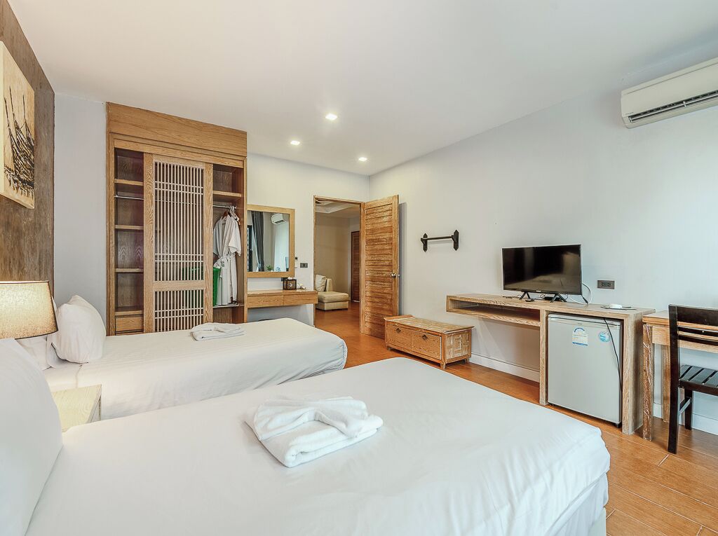 A hotel room with two beds, a desk with a television, a wardrobe, and a small refrigerator.