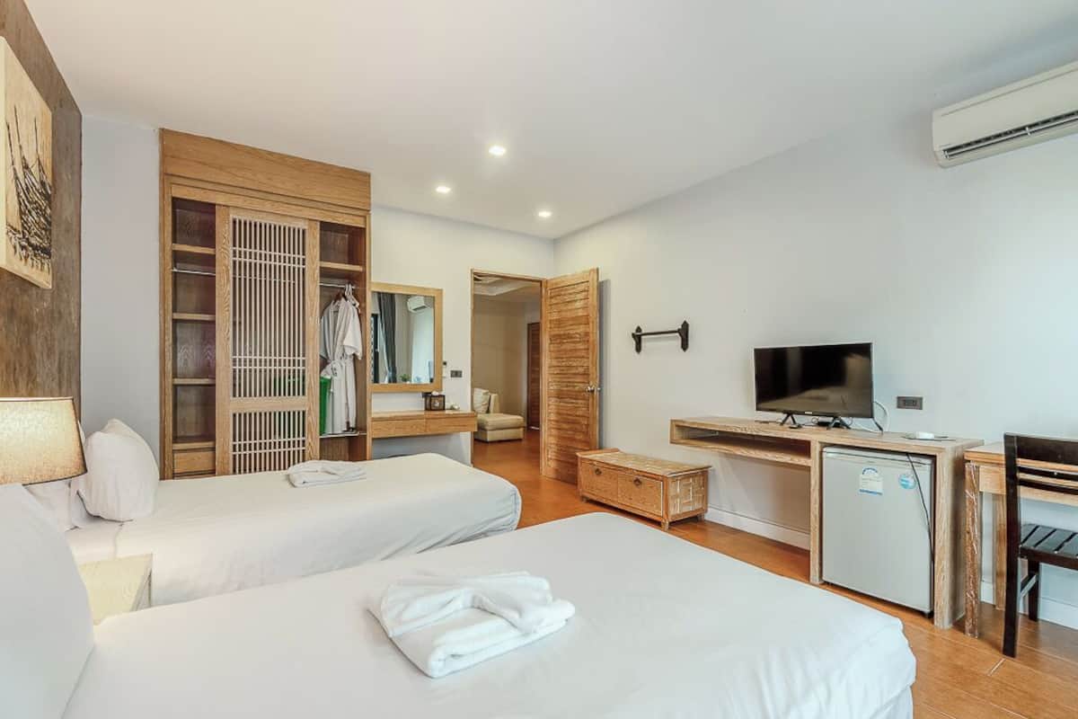 Una habitación de hotel con dos camas, un escritorio con televisor, un armario y un refrigerador pequeño.