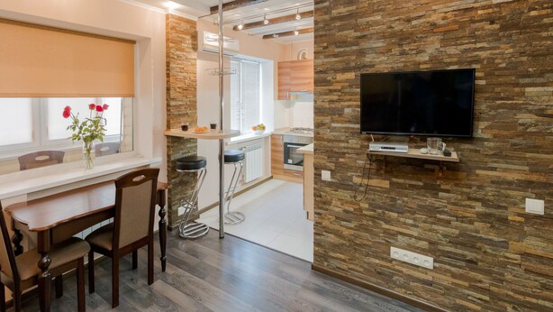 A modern kitchen with a stone wall, a flat-screen TV, and a dining area with chairs and a table. - CityApartments Kyiv Railway Station (Kyiv)