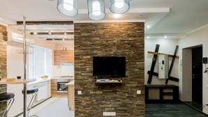A modern kitchen with a stone wall, a TV mounted on it, and a bar area with stools. - CityApartments Kyiv Railway Station (Kyiv)