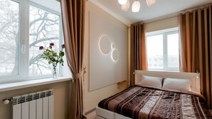 A bedroom with a bed, a radiator, a window with curtains, and a wall-mounted light fixture. - CityApartments Kyiv Railway Station (Kyiv)