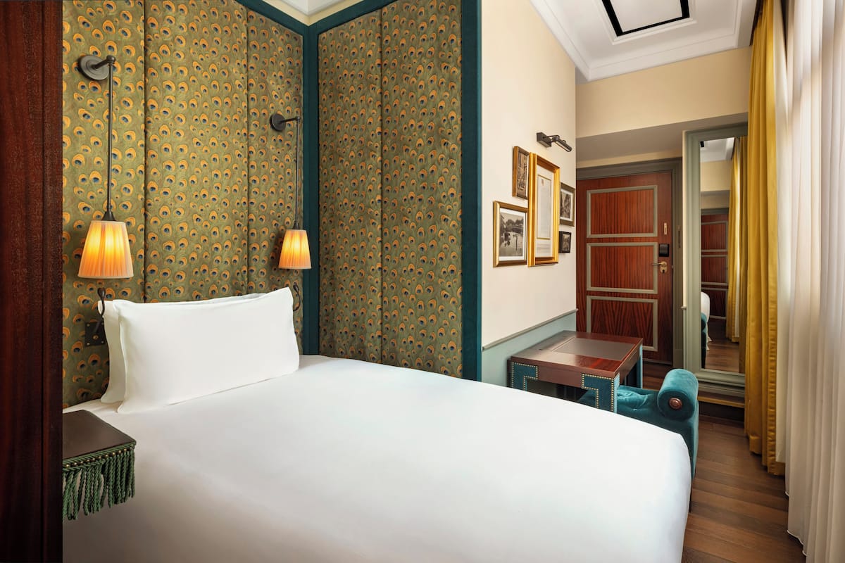 A hotel room with a large bed, two bedside lamps, a small table, and a mirror on the wall.