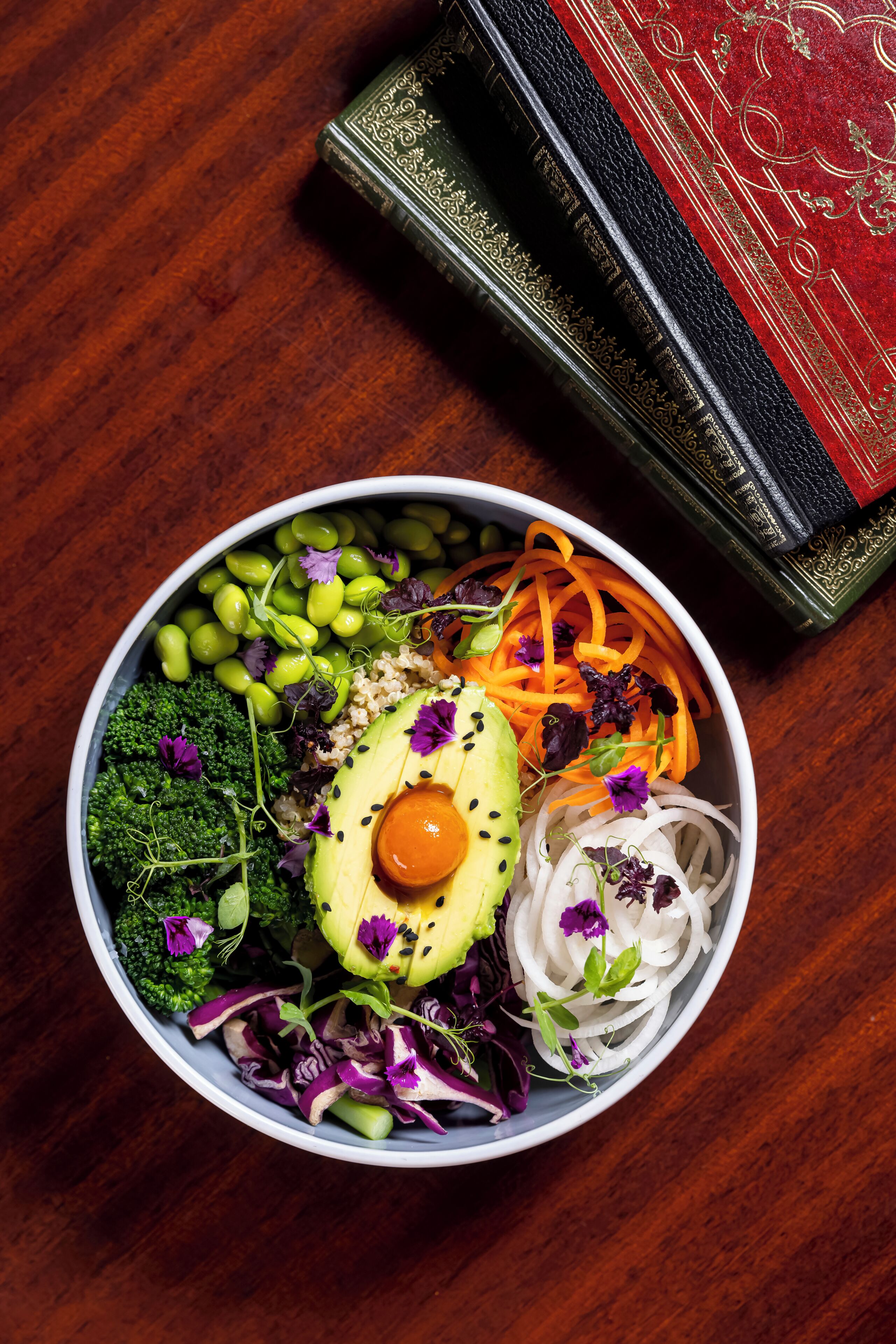 A bowl of salad with various vegetables and a book on a wooden table.