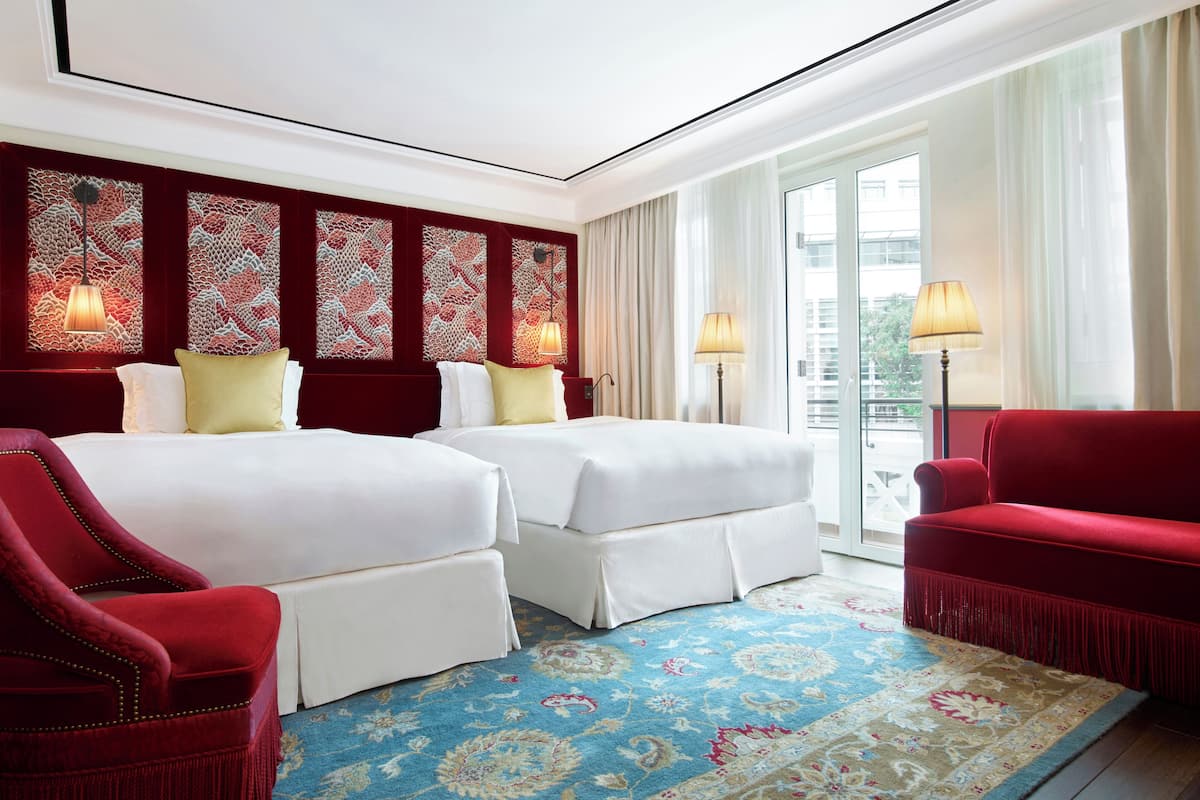 Ein Hotelzimmer mit zwei Betten, einem roten Sessel, einer Stehlampe und einem gemusterten Teppich.