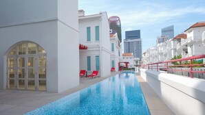 Une piscine avec des chaises rouges, des bâtiments blancs et une structure moderne en verre en arrière-plan.