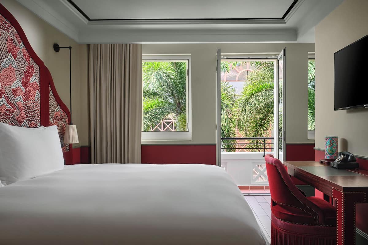 Ein Hotelzimmer mit Bett, Schreibtisch, Stuhl, Fernseher und einem Balkon mit Blick auf Grünflächen.
