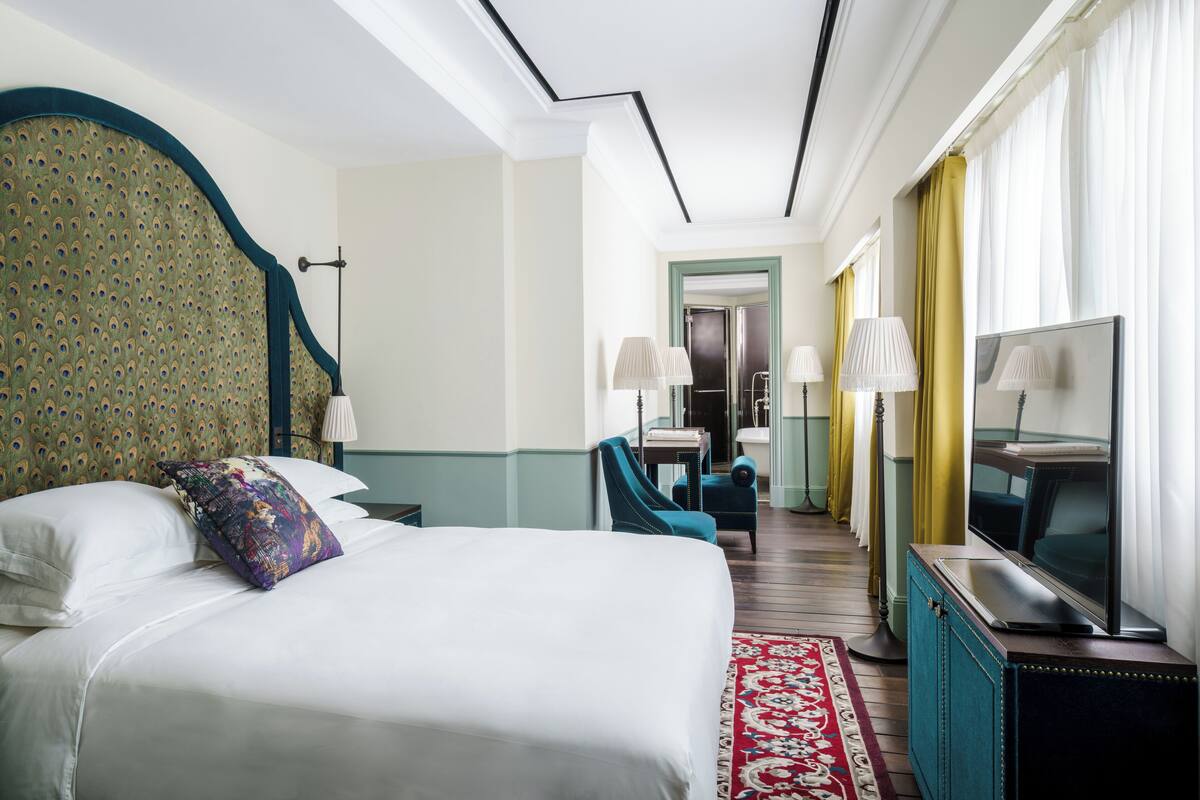 A hotel room with a large bed, a television, a desk, and a chair.