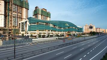 A modern hotel with a curved green roof, multiple floors, and a spacious parking area.