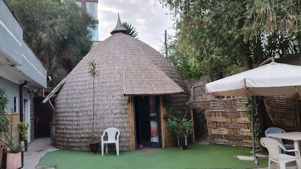 A thatched-roof hut with a door, surrounded by potted plants and a small table with chairs. - Lucy Guest House B&B (Addis Ababa)