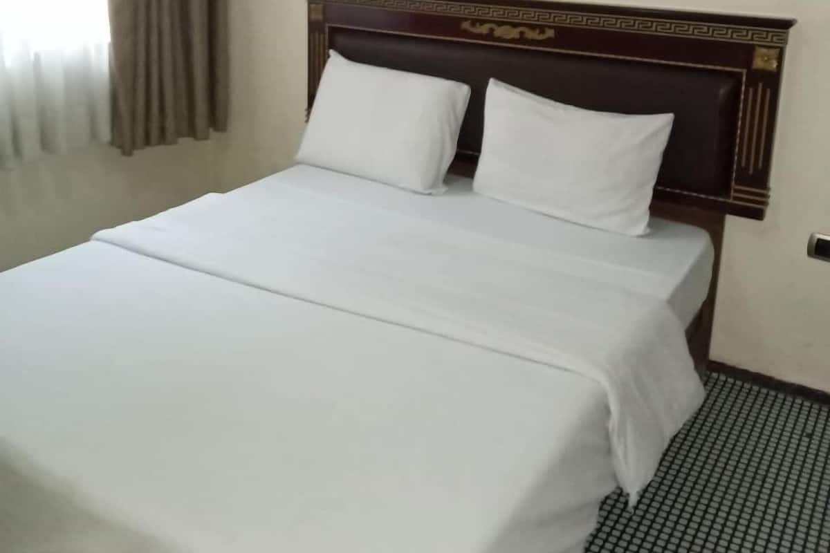 A hotel room with a large bed, a headboard with a decorative pattern, a small bedside table, and a framed picture on the wall.
