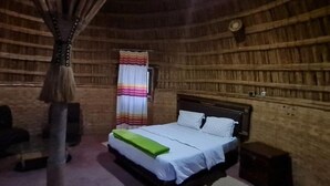 A room with a bed, a chair, a bedside table, a curtain, and a wall clock. - Lucy Guest House B&B (Addis Ababa)