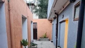A narrow alleyway between buildings with potted plants and a blue water container. - Lucy Guest House B&B (Addis Ababa)