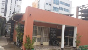 A modern building with a pink facade, large windows, and a covered entrance area with potted plants. - Lucy Guest House B&B (Addis Ababa)