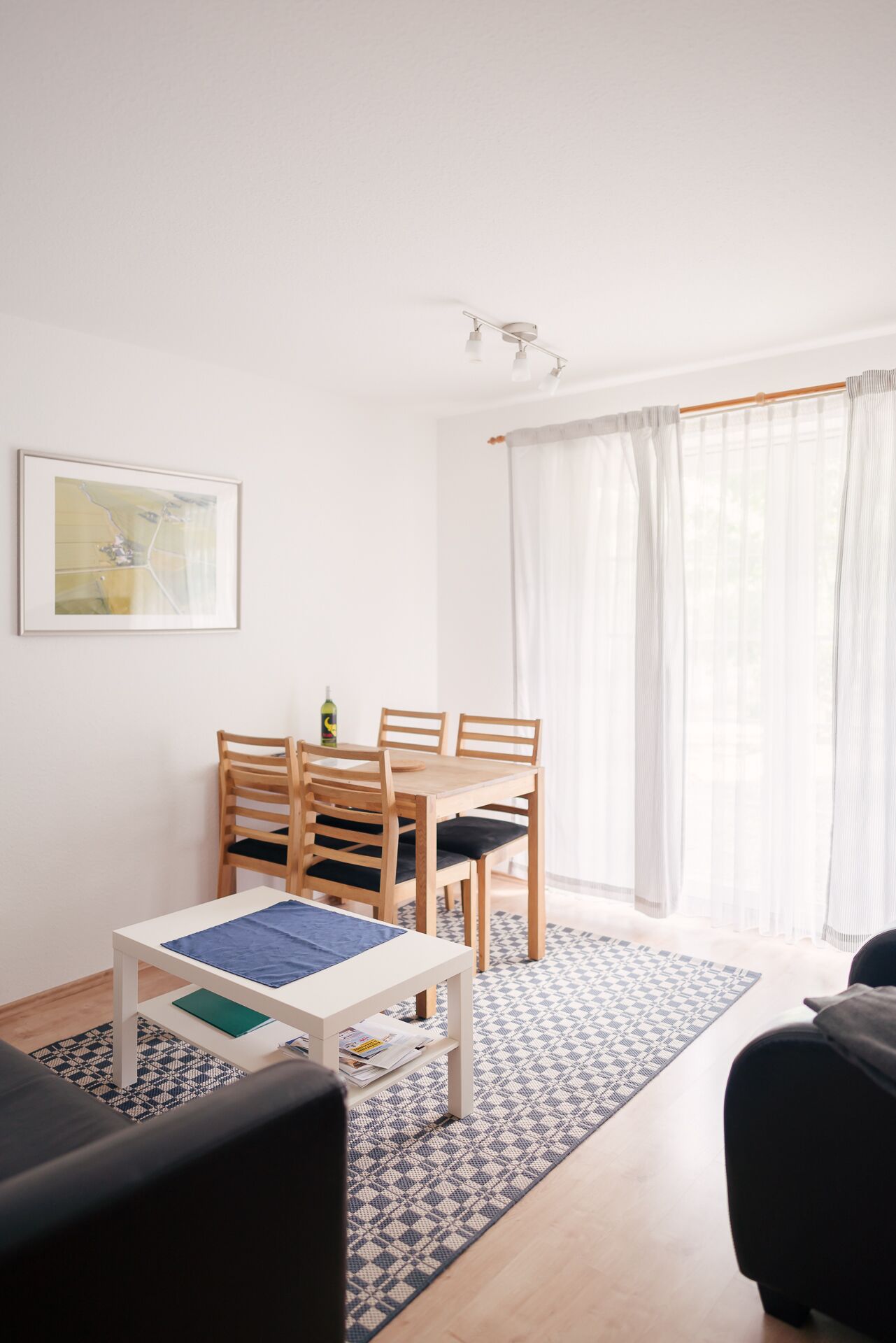 Un soggiorno moderno con zona pranzo, caratterizzato da un tavolo bianco, sedie in legno, un divano nero e un tappeto decorato.