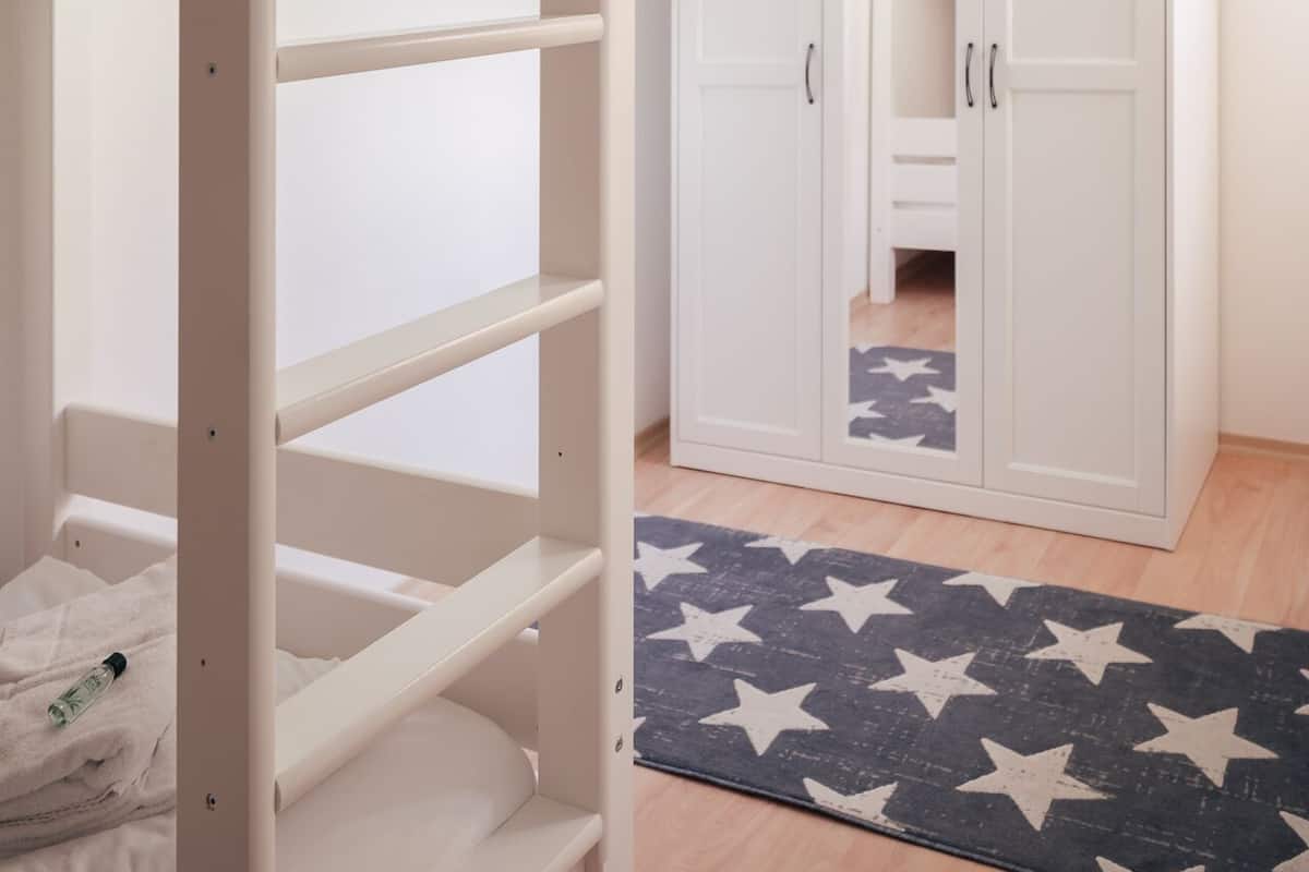 Ein Stockbett mit einem Kleiderschrank und einem Teppich mit Sternenmuster in einem Zimmer mit Holzboden.