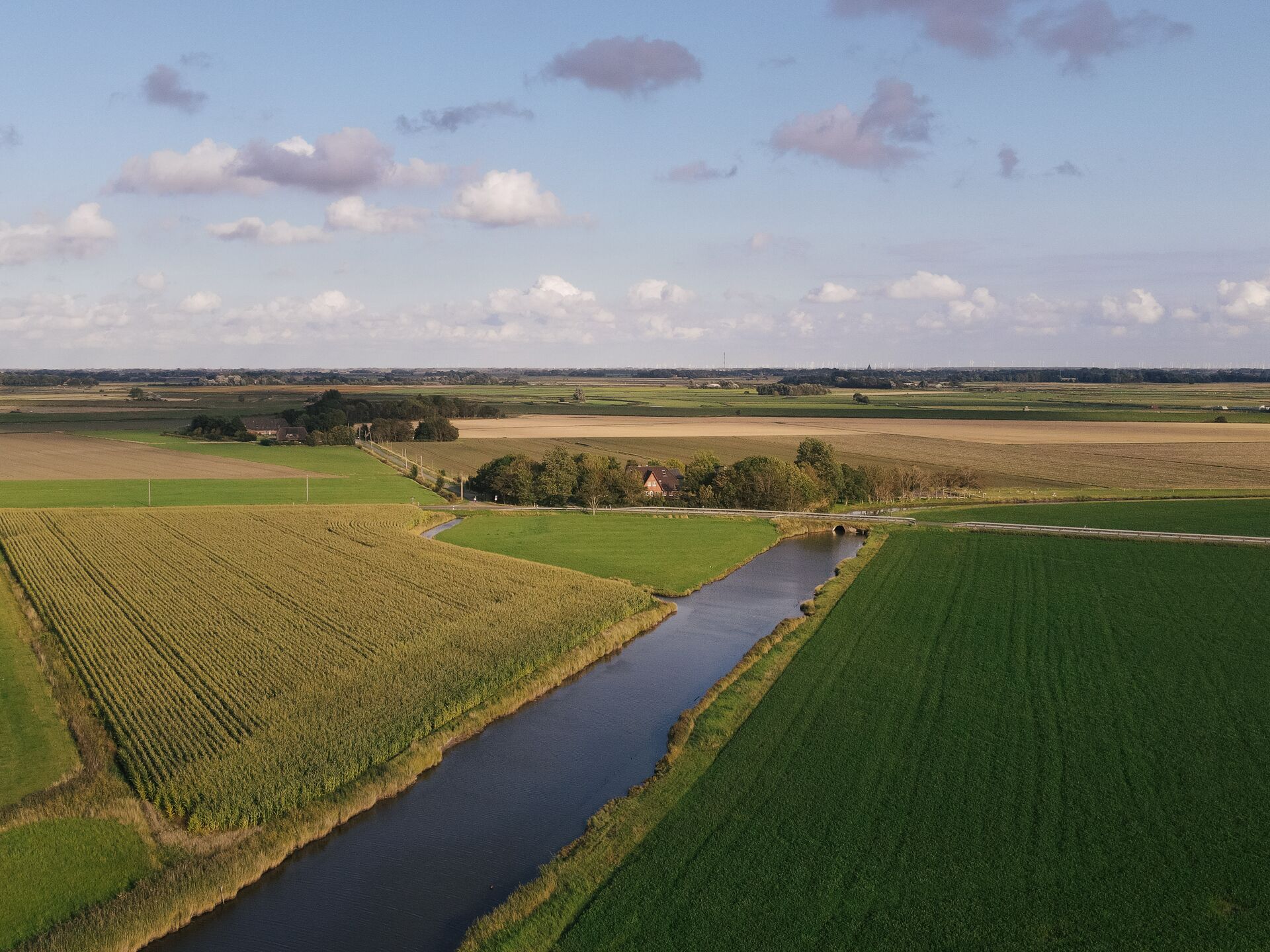 A rural landscape with a river, fields, and a distant wind farm.