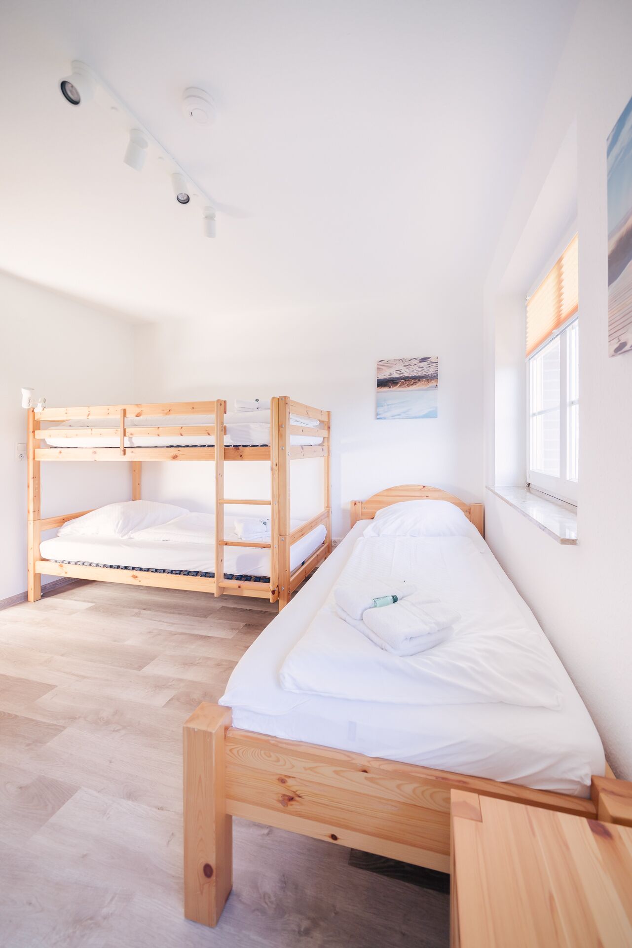 A dormitory room with bunk beds, a window with blinds, and a painting on the wall.