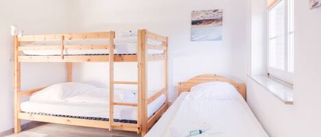 A dormitory room with bunk beds, a window with blinds, and a painting on the wall.