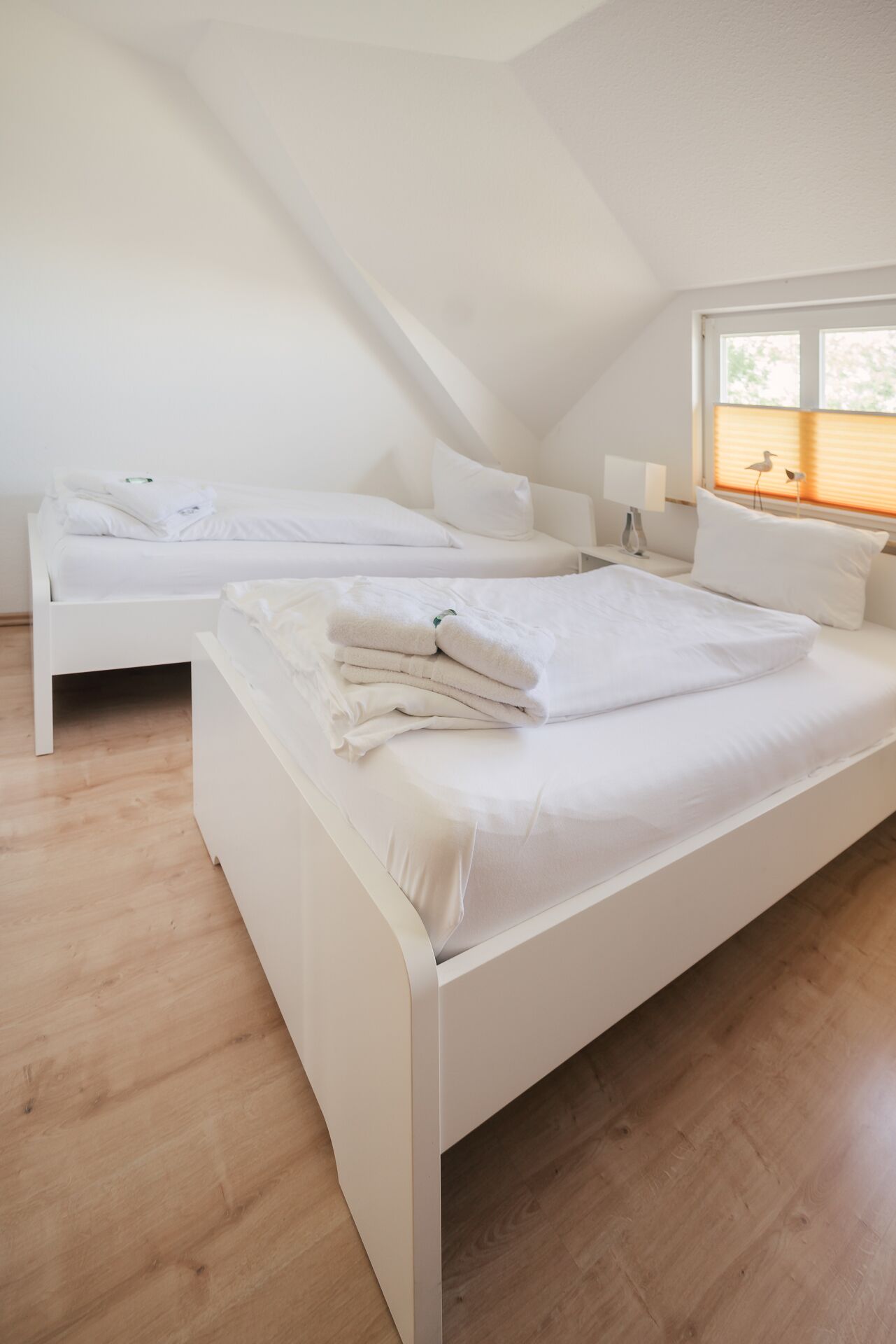 Une chambre moderne, décorée dans des tons de blanc, avec deux lits, une lucarne et une vue sur l’extérieur.