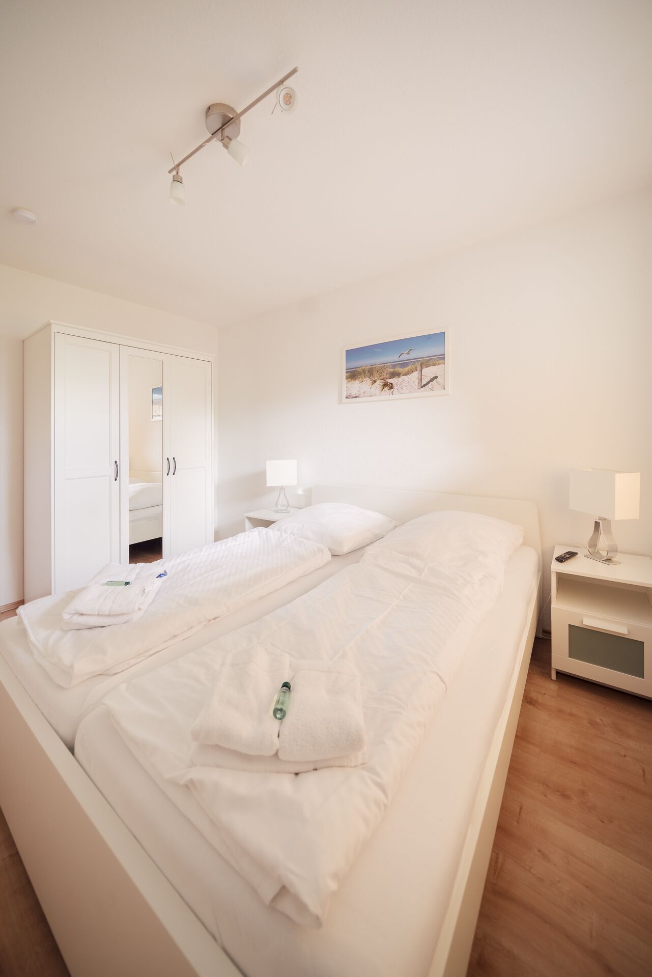 A bedroom with a large bed, a wardrobe, a bedside table with a lamp, and a wall-mounted picture.