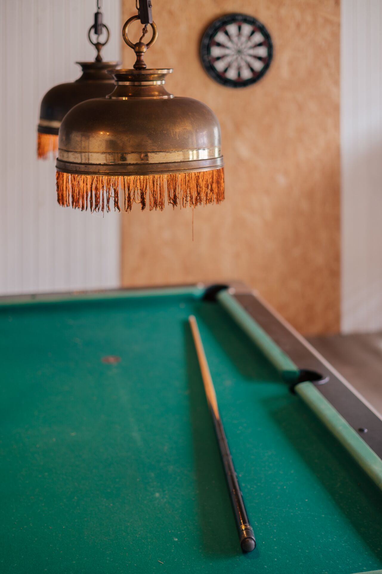 A pool table with a cue stick and a hanging lamp.