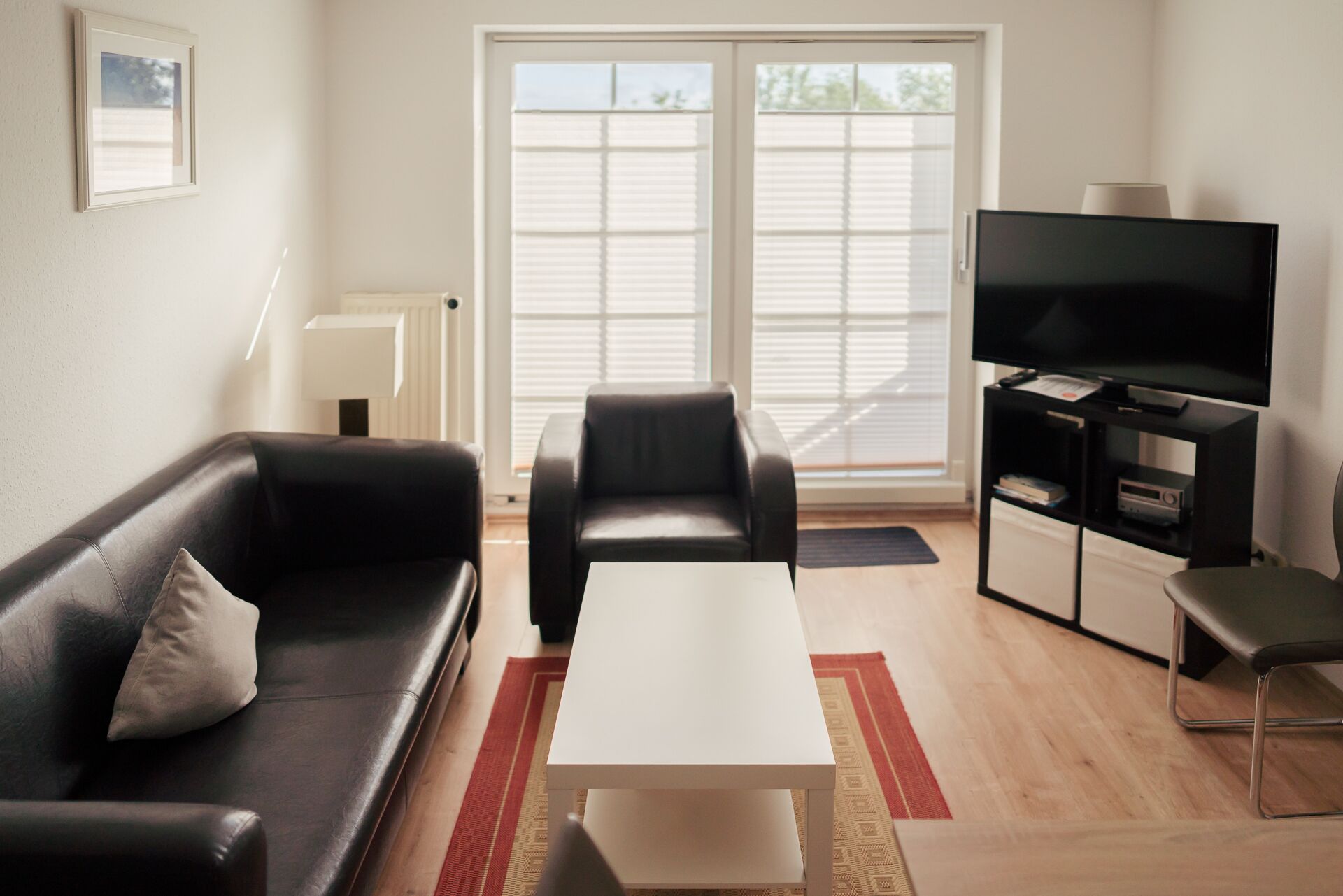 A modern living room with a black leather sofa, a white coffee table, a black armchair, and a TV on a black stand.