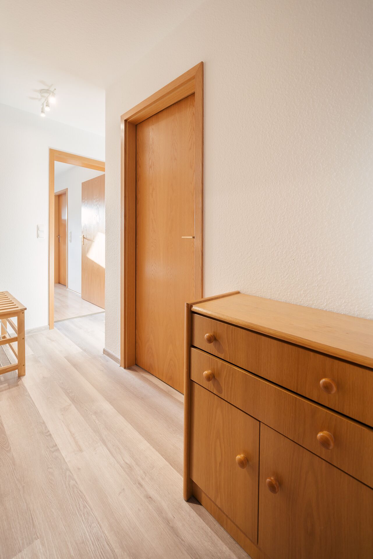 Un pasillo con una puerta de madera, un armario de madera con cajones y una mesa de madera.