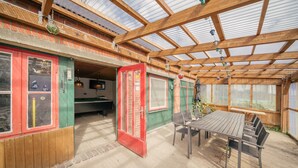 A covered patio with a pool table, wooden furniture, and a greenhouse structure. - FEWO auf dem Lande (Tumlauer Koog)
