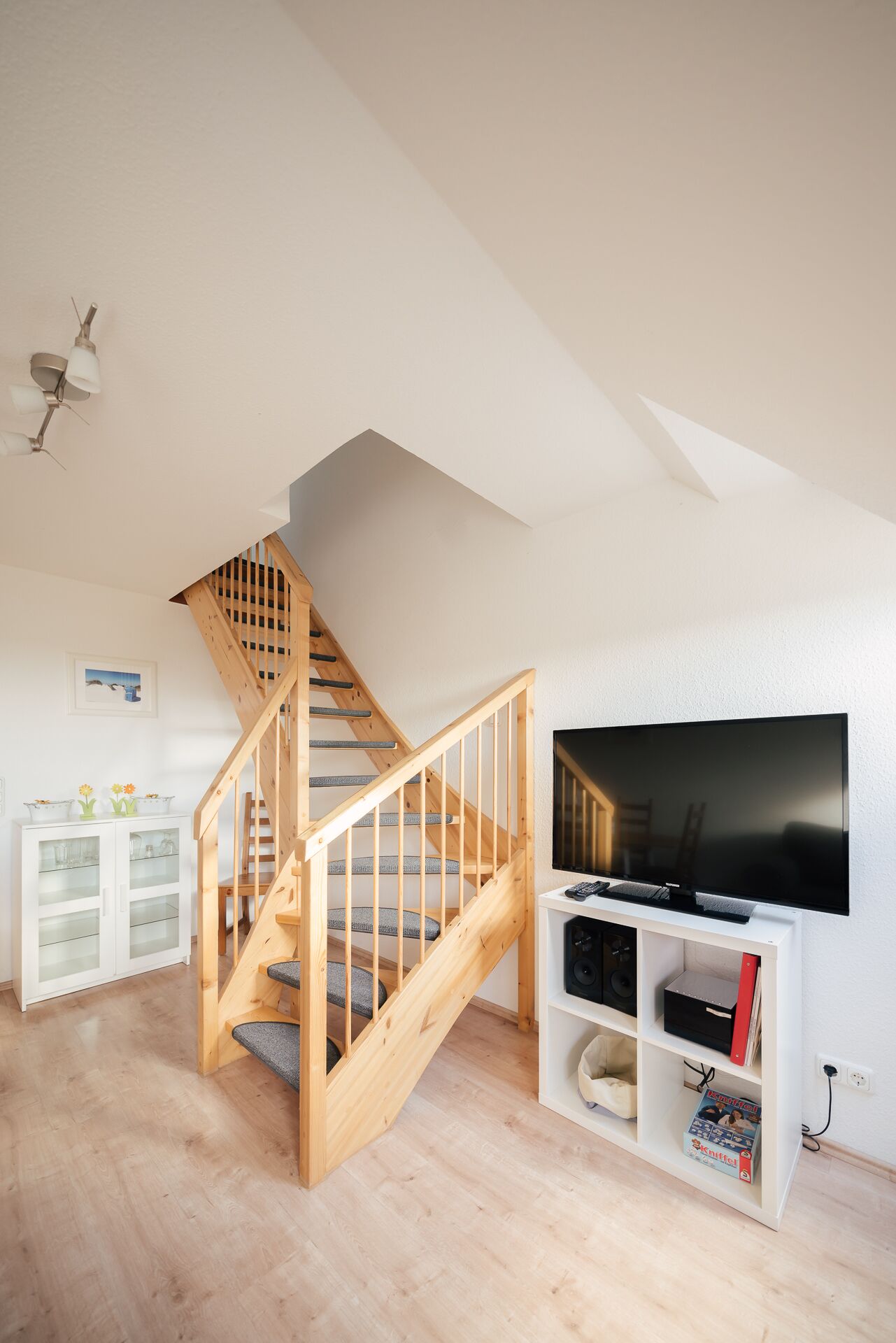 A spacious room with a wooden staircase, a flat-screen TV, and a white cabinet with glass doors.