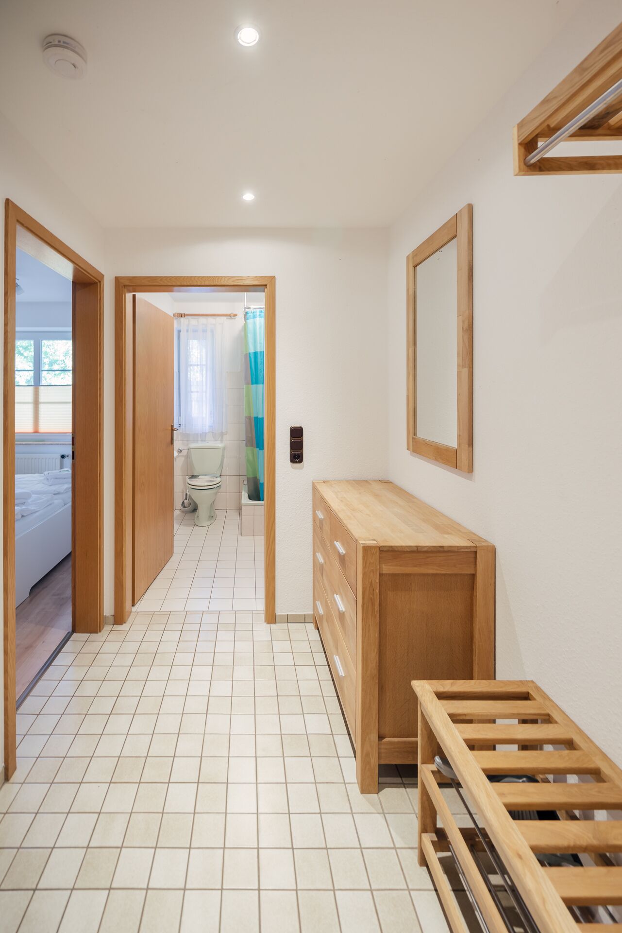 Ein Flur mit einer hölzernen Sitzbank, einem Spiegel und einer Toilette mit Duschvorhang.
