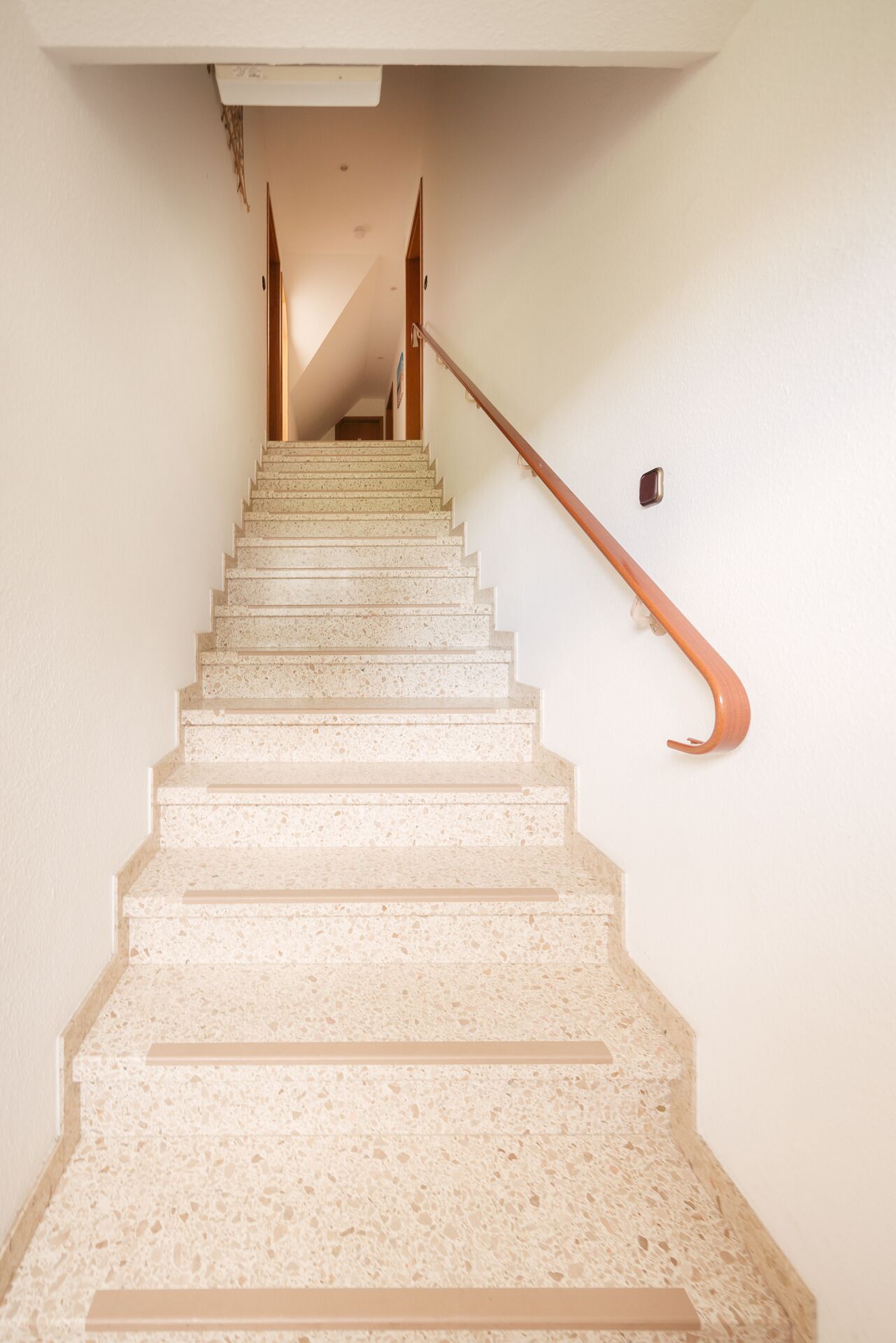 A staircase with a wooden handrail and a wall-mounted light fixture.