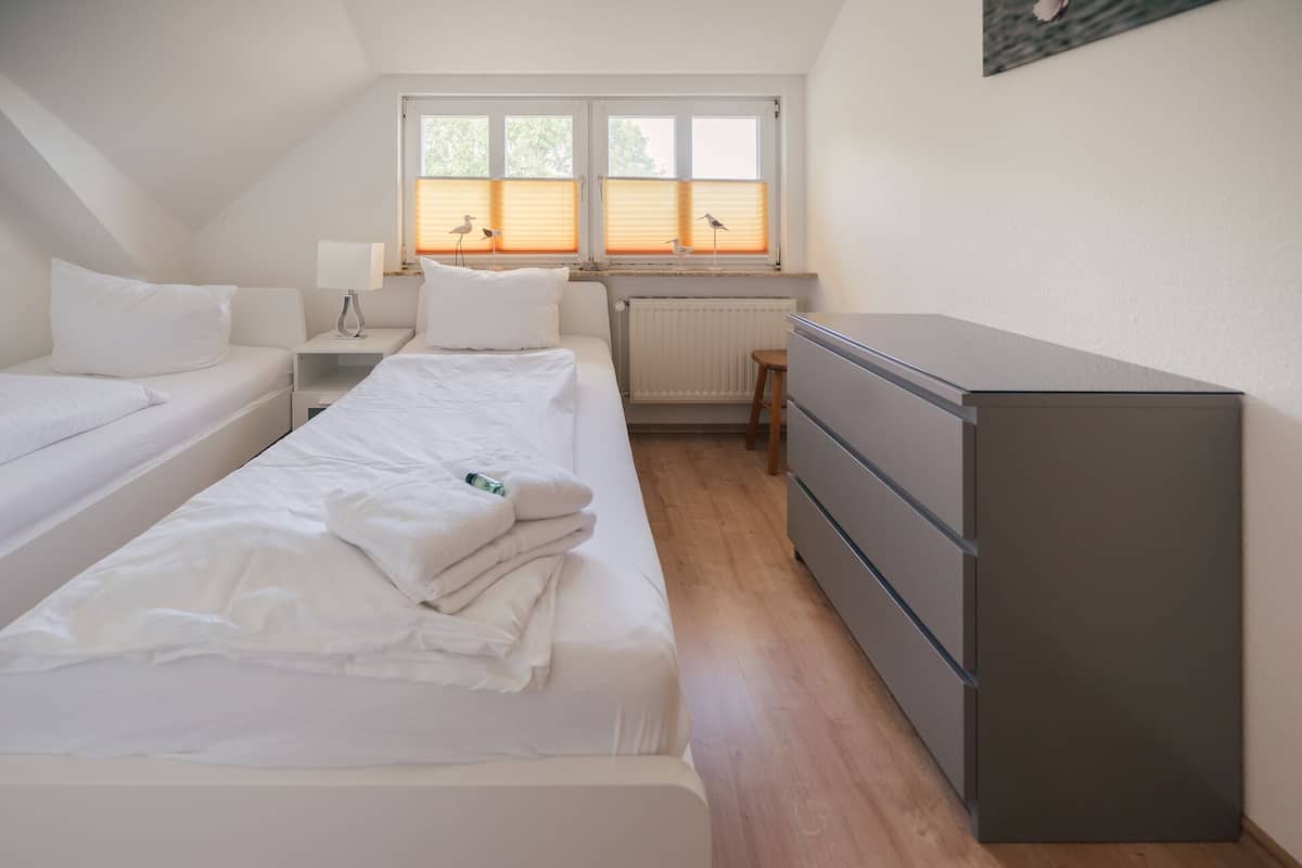 Ein kleiner, sauberer Raum mit zwei Betten, einem Schminktisch, einem Heizkörper und einem Fenster mit Jalousien.