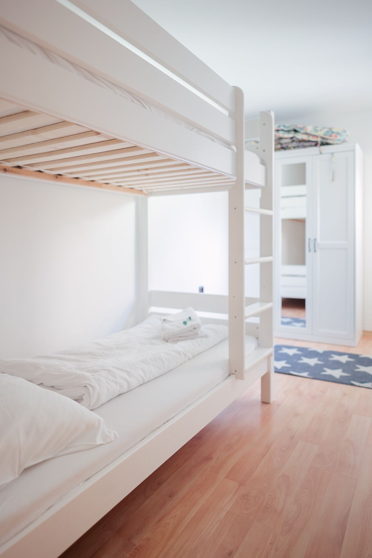 A bunk bed in a room with wooden flooring, white walls, and a window.
