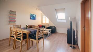 A cozy loft apartment with a dining area, a sofa, a TV, and a window.